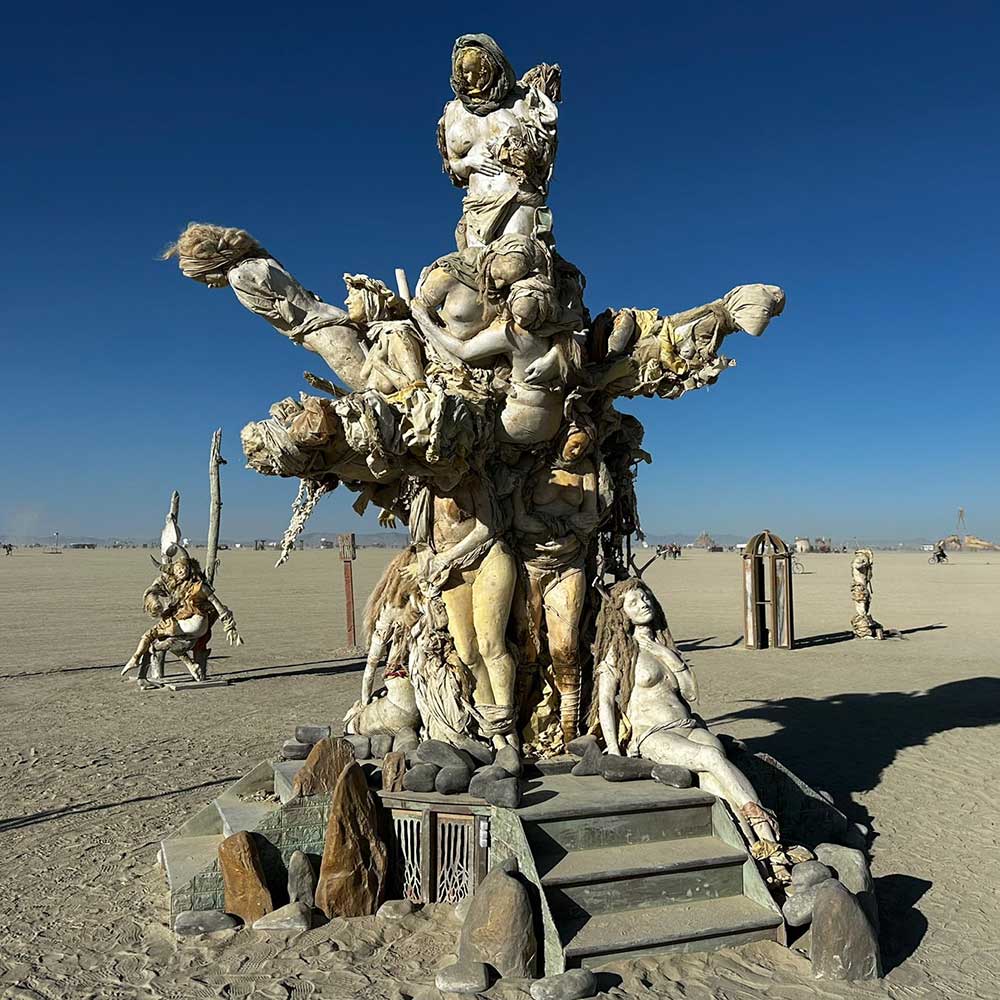 Womantree by day, a tree formed from cast figures of women rising above stone steps under a deep blue sky