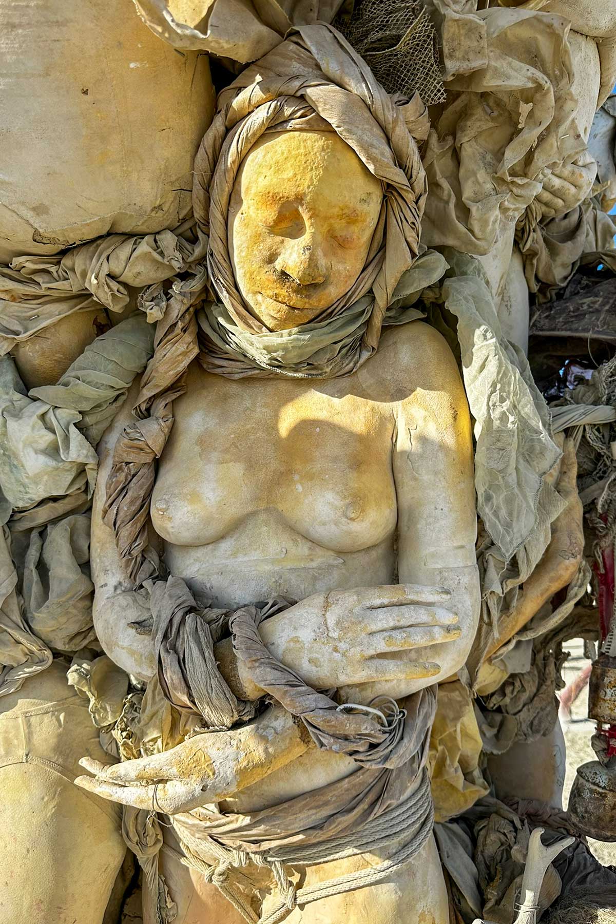 Close-up of a cast woman in a headscarf, eyes closed and hand resting on her chest, nestled in the trunk