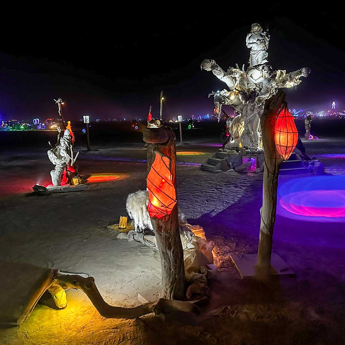 Womantree at night, with red lanterns glowing on posts and pools of purple light across the playa