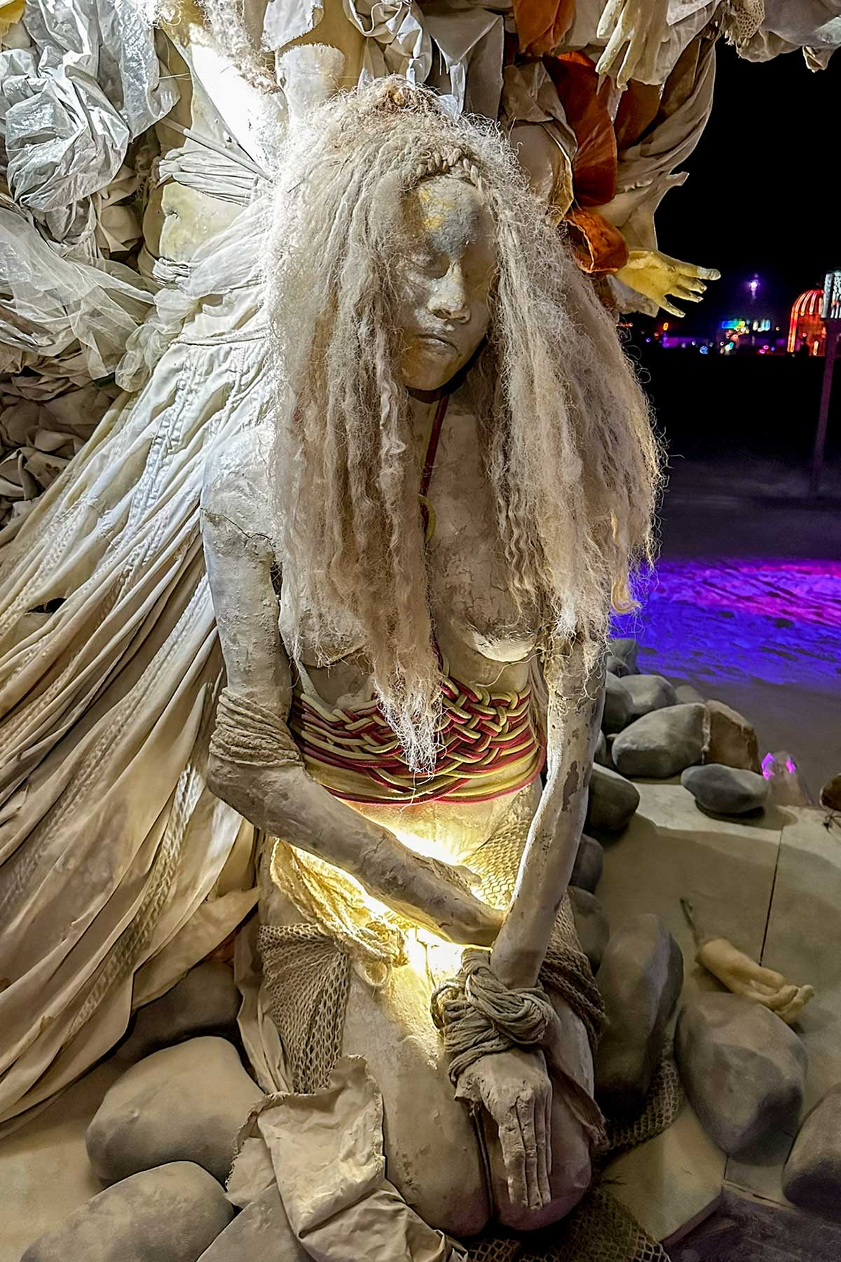 Close-up at night of a cast woman with long, pale hair, softly lit from below