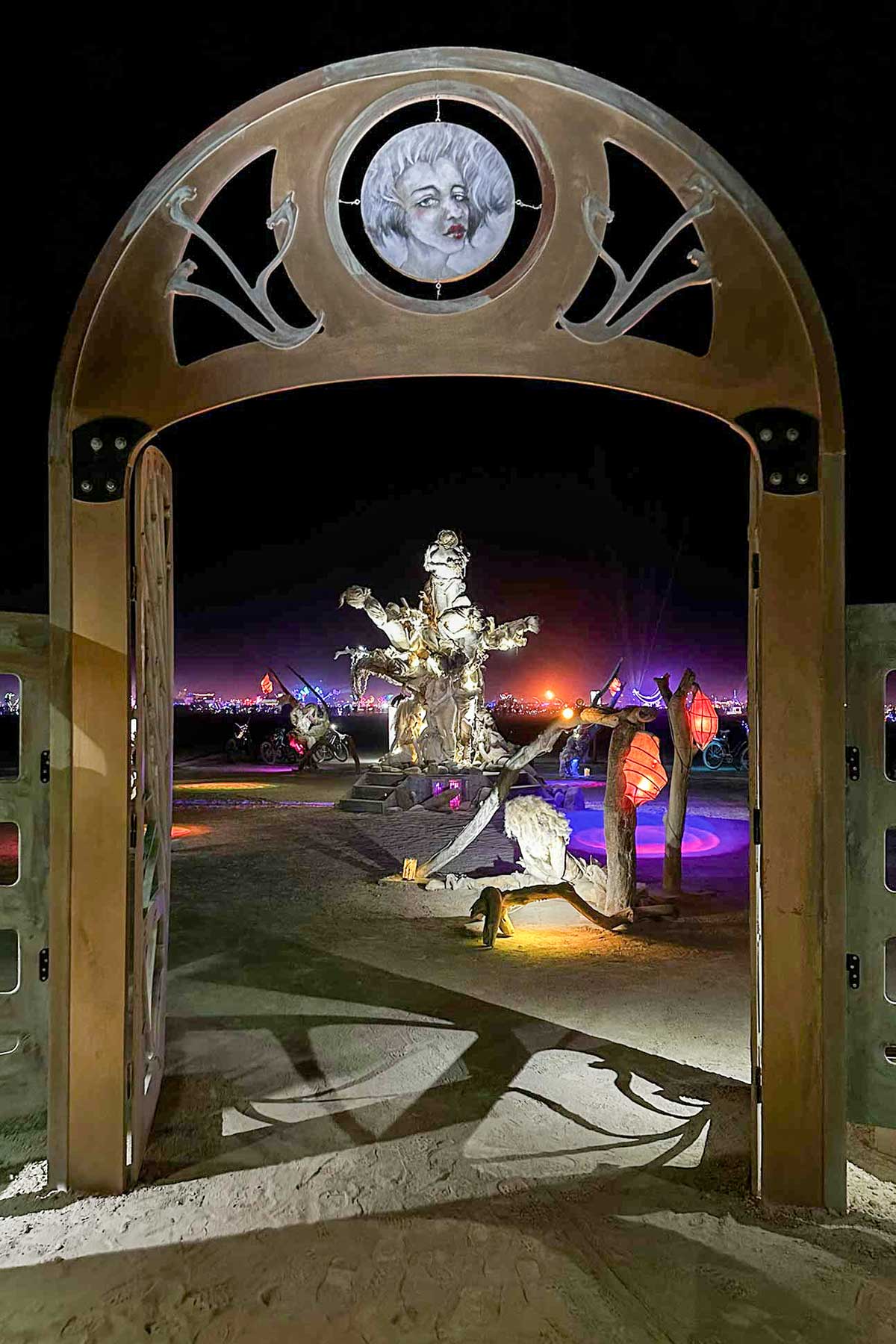 Arched gateway with its face medallion at night, framing the illuminated Womantree beyond