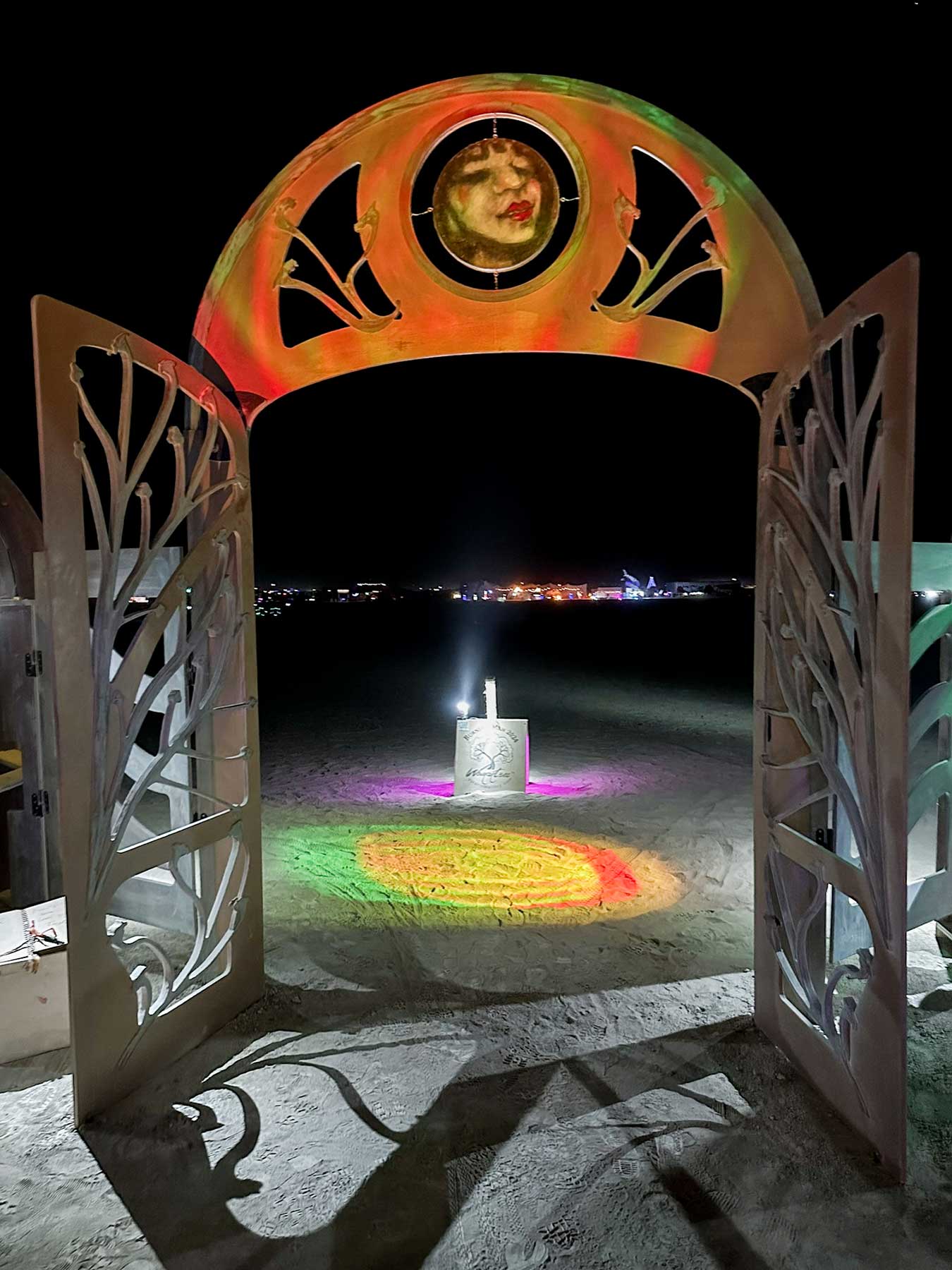 Gateway washed in orange and red light at night, its ornate open doors framing a glowing light post