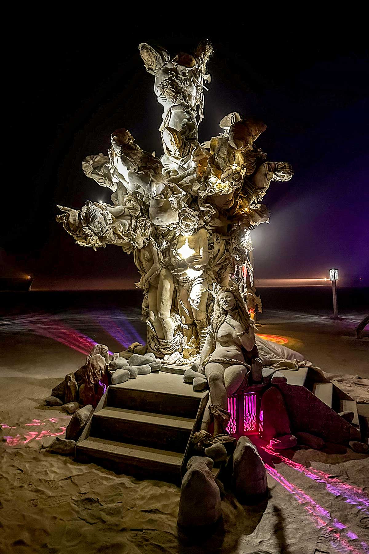 Womantree lit from within at night, beams of light cutting through the dust