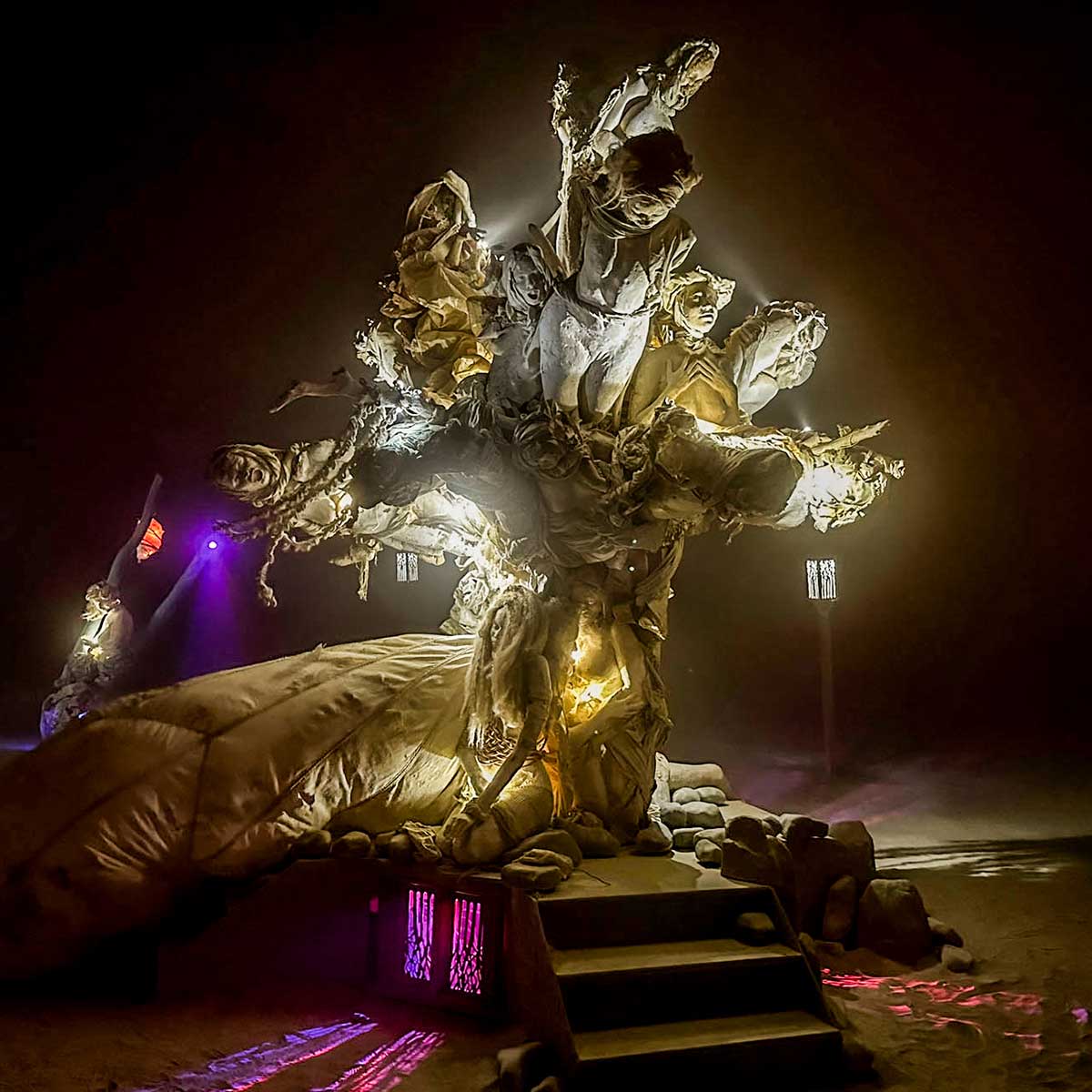 Womantree glowing at night, its branches of cast figures spreading above a draped base