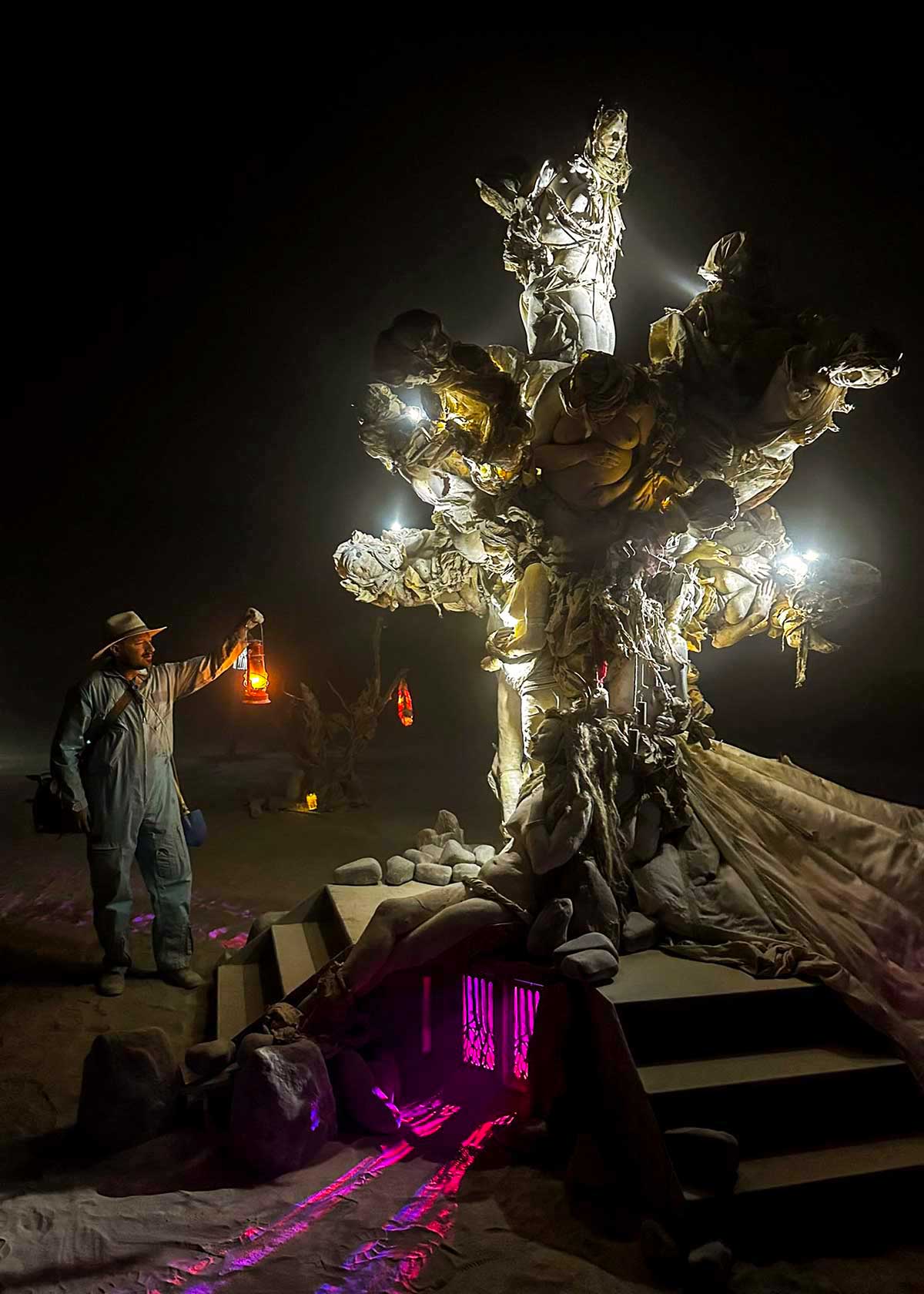 A visitor holding a lantern stands beside the glowing Womantree at night