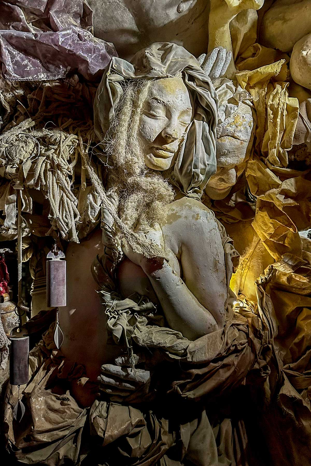 Close-up at night of a cast woman with eyes closed, embracing a figure within the folds of the trunk