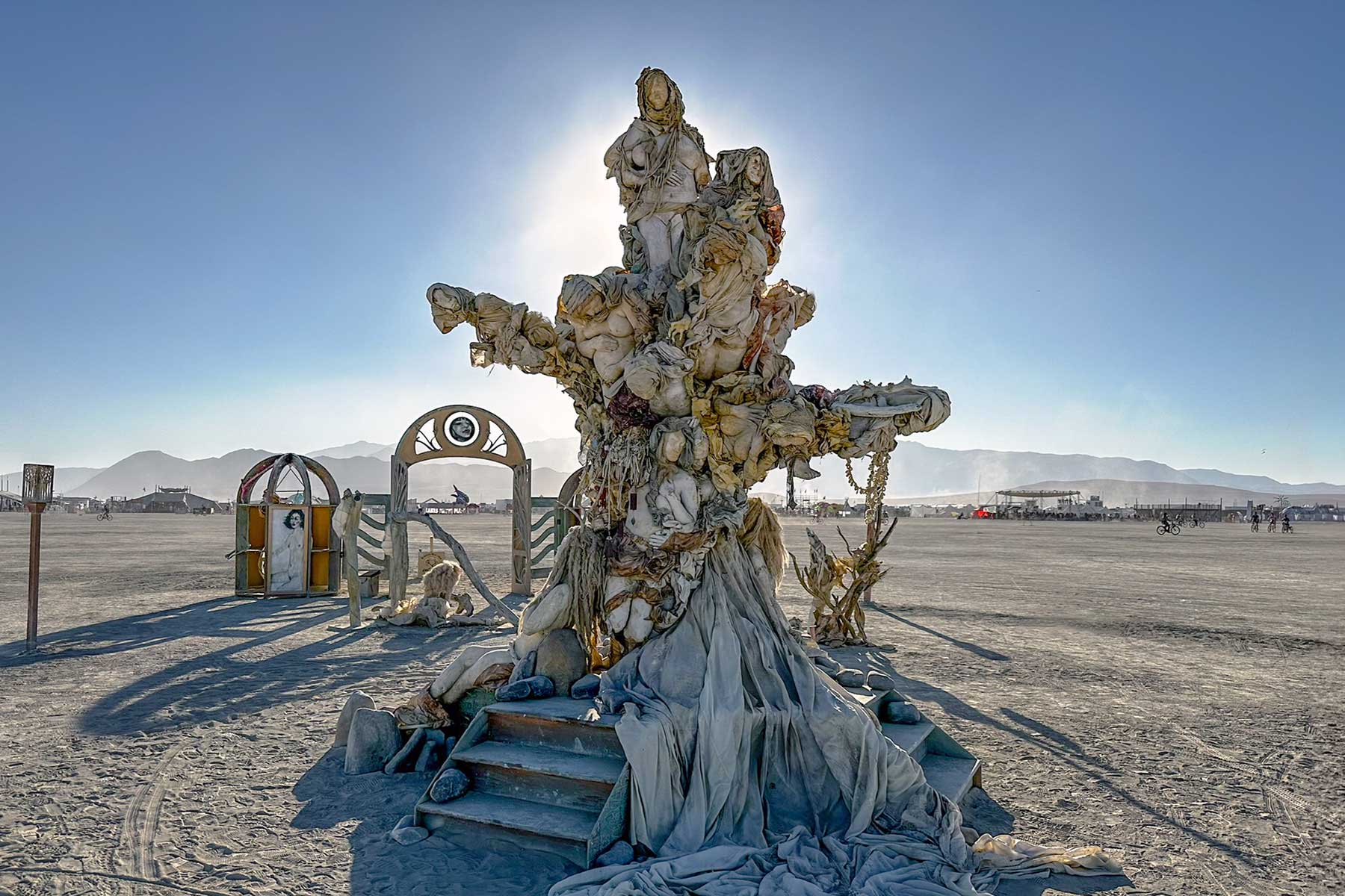 Womantree backlit by the sun on the playa, with the arched gateway and portrait kiosks behind it
