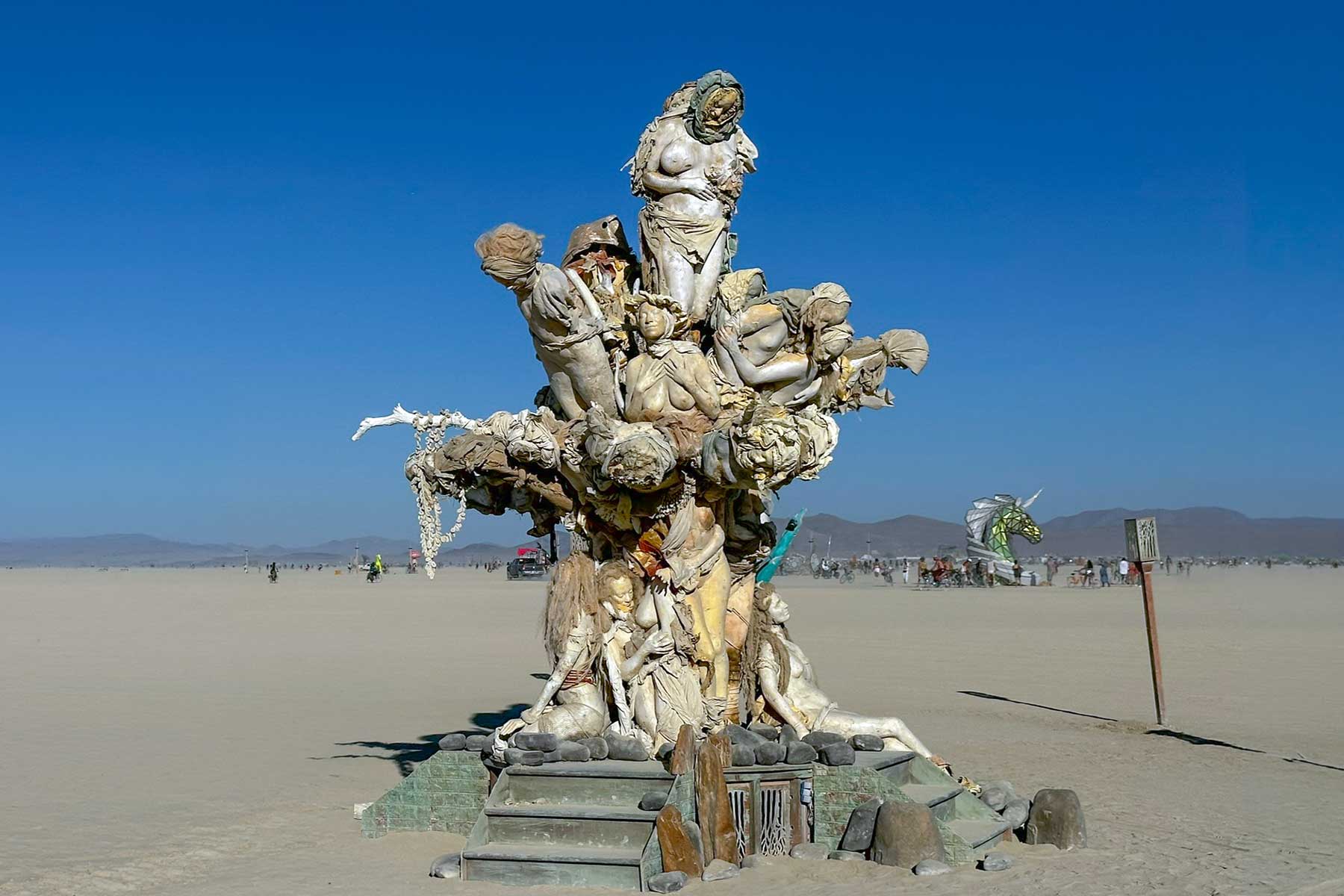 Womantree by day, a tree formed from cast figures of women rising above stone steps under a deep blue sky
