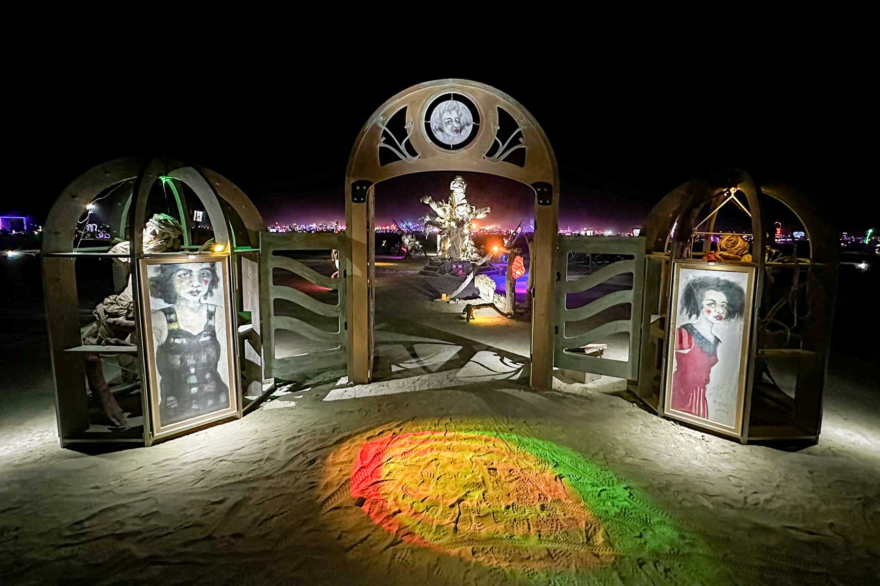 Womantree's entrance at night: the illuminated arched gateway between two portrait kiosks, with the tree glowing beyond